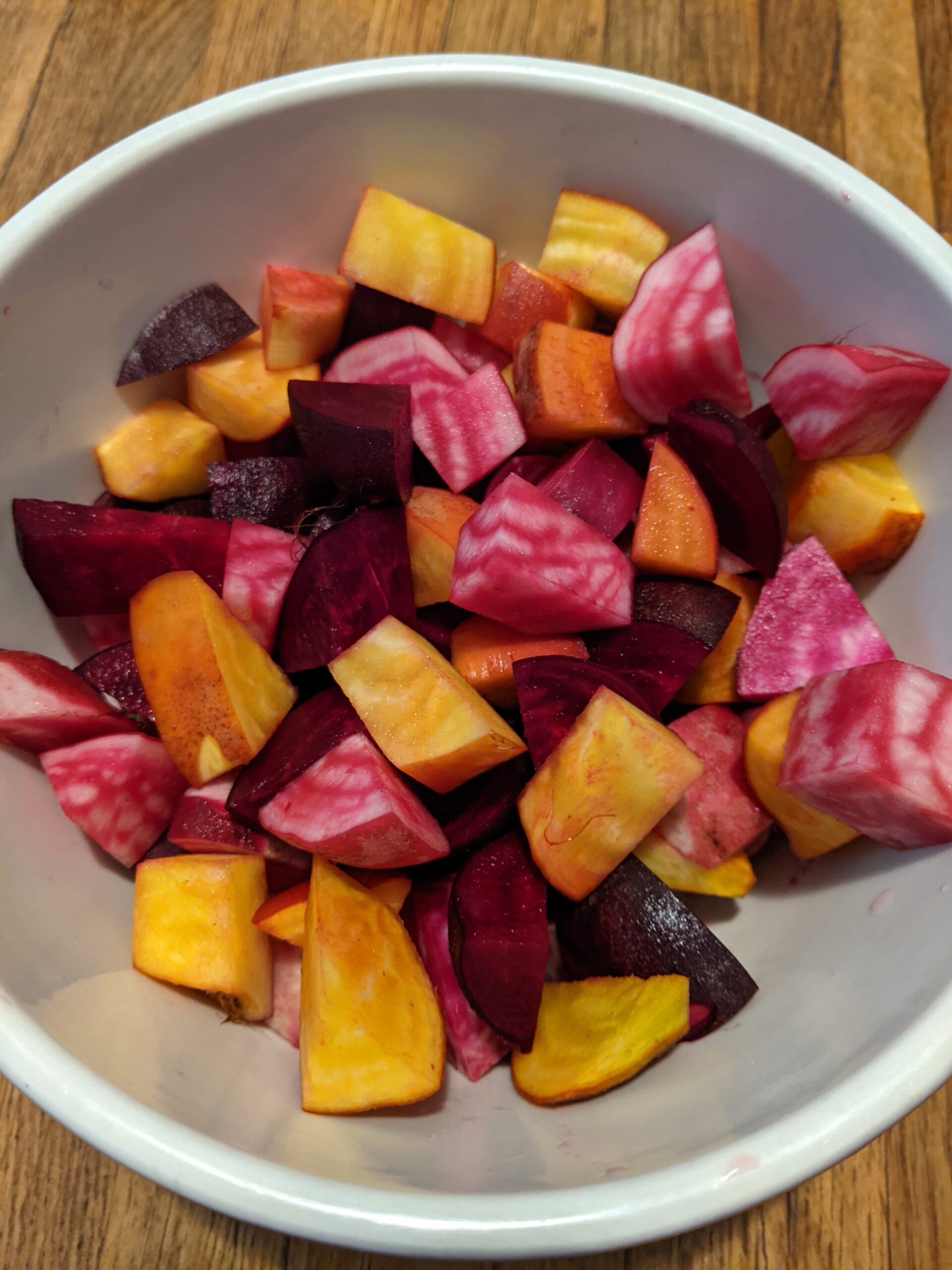 A white bowl holds three different colors of beets: golden, bull's blood red, and chiogga, which has pink and white stripes