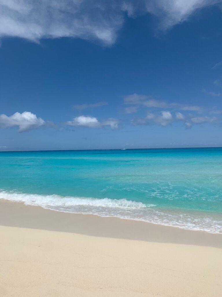 A beach with blue water,  with a few clouds in the sky. 