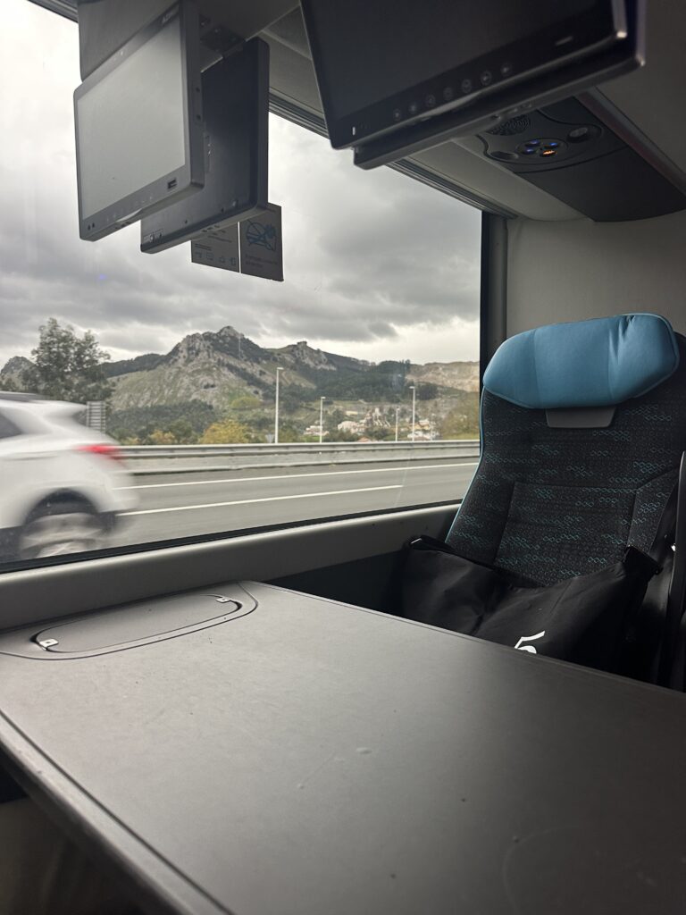 Bus seat and table. Bus window with landscape in the background. green mountains and cloudy sky.