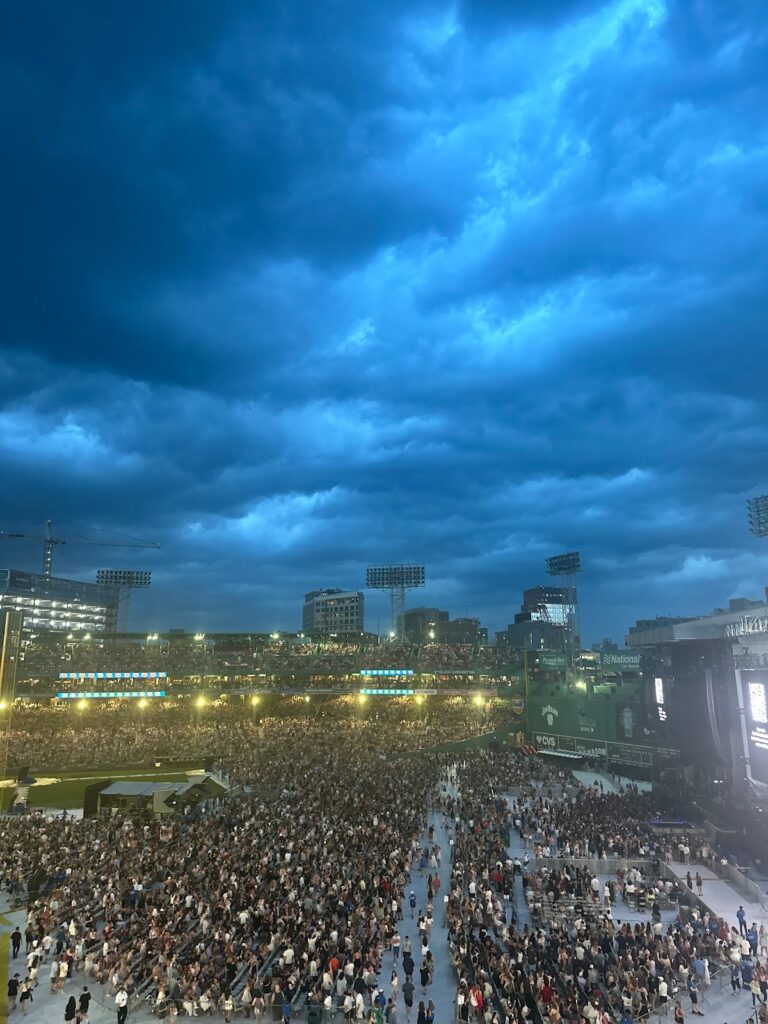 dark blue and gray clouds fill the sky, overlooking a filled Fenway park at dusk.